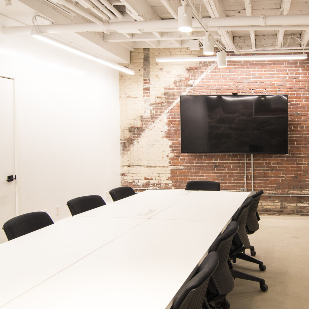 Brightly-lit large meeting room with tables, chairs, whiteboard walls, and large screen television.