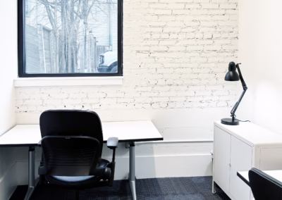 White brick office with two desks and large window.